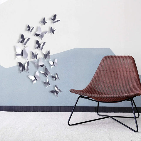 3D Mirror Butterfly Wall Decor Kit With 48 Removable Stickers in Silver Finish displayed above a chair on a wall