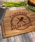 Front view of engraved wooden cutting board with Campbell Steak House logo, knife, asparagus and herbs