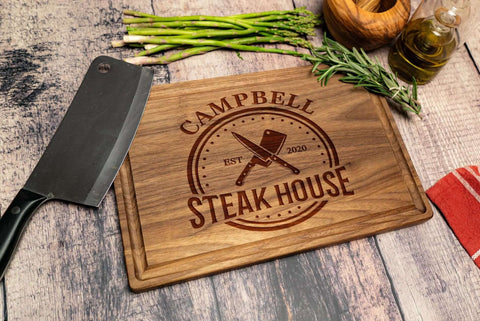Front view of engraved wooden cutting board with Campbell Steak House logo, knife, asparagus and herbs