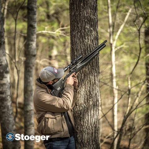 Hunter aiming XM1 Scout Compact PCP Air Rifle Caliber Twenty Five With Black Synthetic Stock in forest setting