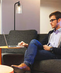 Industrial Floor Lamp With Hanging Glass Shade In Black Farmhouse Vibe next to a man working on a laptop in a cozy living room