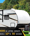 12V electric RV tongue jack, black, mounted at the front hitch of a white travel trailer.