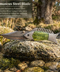 Fish Style Copper Damascus Folding Knife With Ladder Pattern Blade, Brass Engraved Handle, on a rock near stream