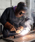 Cowhide Welding Cape Jacket Built Like A Tank Featuring Full Cape Sleeves Anchored To A Heavy Duty Bib Apron For Top Tier Heat And Spark Shielding In Pitch Black worn by a welder.  