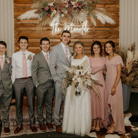 Wedding party poses in front of 'The Mendozas' sign with floral decor and wooden backdrop.
