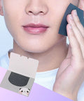 Man using dual pack oily skin blotting sheets, holding one against his face, panda design packaging visible.