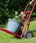Red hand truck with 10x3.00-4 flat free tire and wheel assembly carrying large planter, showing side view on grass
