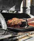 Person handling hot meat on grill wearing BBQ Glove Set With Four Cotton Liners And One Hundred Black Nitrile Gloves.