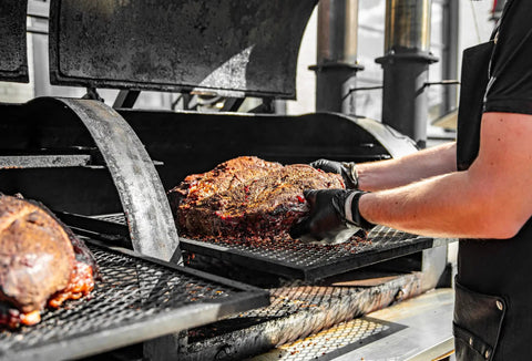 Person handling hot meat on grill wearing BBQ Glove Set With Four Cotton Liners And One Hundred Black Nitrile Gloves.