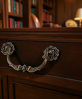 4-Pack Antique Brass Drawer Pulls 4.5 Inch Center-to-Center Drop Bail Dresser Handles Vintage Style Bronze Look Hardware for Cabinets Desks and Dressers 107mm Centers Zinc Alloy Construction Durable Ornate Finish installed on a wooden drawer in a classic study room.