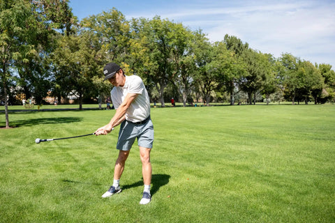 Golfer using Pin Point Golf Swing Tempo Trainer And Warm Up Club With Flexible Shaft For Lag Training, Counter Balanced Weighted Ball Head, Warm Up And Practice Accessory For Swing Improvement, Black on grass field.