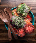 Fresh salad with microgreens, tomatoes, toast, and wooden utensils on a wooden table, featuring Colorful Microgreen Seeds Mix for Home Growers.