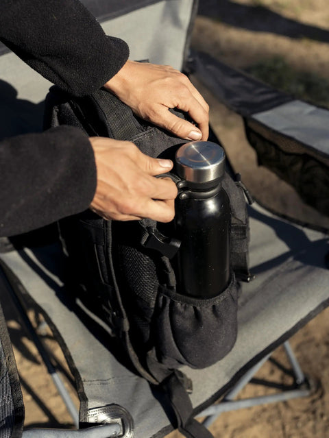 Person placing a bottle in Wakizashi Tactical Backpack 24L With MOLLE System Durable 100 Percent Polyester Gear Pack For EDC Outdoor And Tactical Use 17.1 By 11.1 By 6.1 Inches Black on a chair