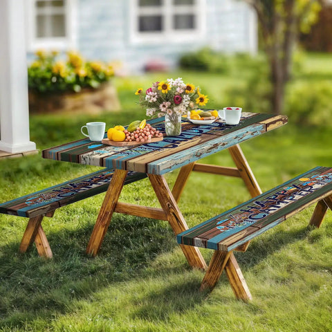Wooden picnic table set in backyard with colorful table and bench covers, floral centerpiece, cups, and snacks for outdoor dining.