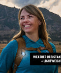 Smiling hiker with Moonlit Rechargeable Micro Lantern for Camping and Hiking attached to backpack, mountains in background.