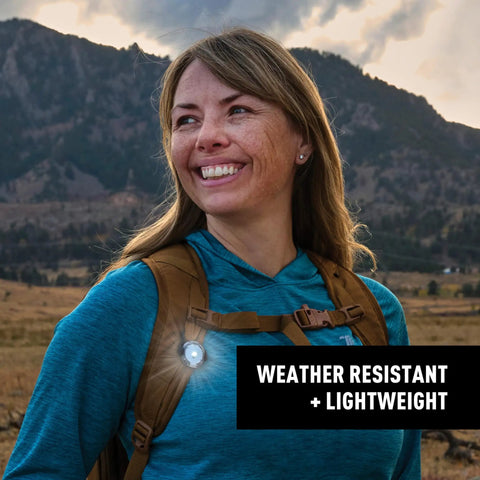 Smiling hiker with Moonlit Rechargeable Micro Lantern for Camping and Hiking attached to backpack, mountains in background.