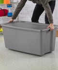 Person lifting Go Big On Storage With This 50 Gallon Gray Bin Featuring Heavy Duty Latches And Secure Recessed Lid And Extra Large Stackable Plastic Tote Built Tough For Moving Bulk Gear And Closet Hauls.