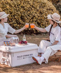 Heavy Duty Rolling Bin With Secure Lid And Easy Roll Casters, stacked with drinks on top, girls enjoying picnic in nature.