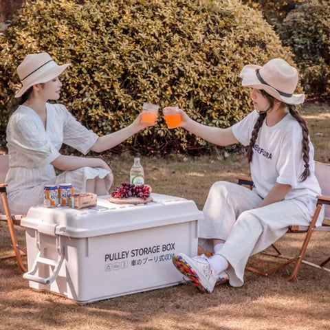 Heavy Duty Rolling Bin With Secure Lid And Easy Roll Casters, stacked with drinks on top, girls enjoying picnic in nature.