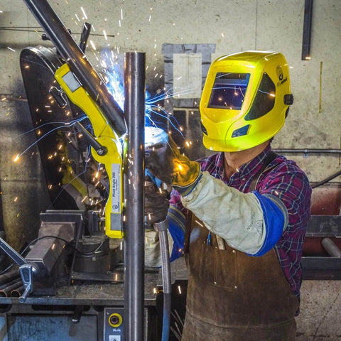 Pivot Angle 200 welding magnet in yellow clamps a metal pipe for welding, used by worker wearing a yellow helmet.