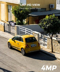 Aerial view of a yellow car parked on a residential street beside a house with a fence and trees, showcasing 4MP HD image quality.