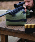 Pre Filled All Weather Rifle Sandbag Rest For Bench Shooting And Competition Front And Rear Set Ready To Use Heavy Duty 900D Oxford Fabric Tear Resistant Olive Drab on wooden table with scope mounted rifle