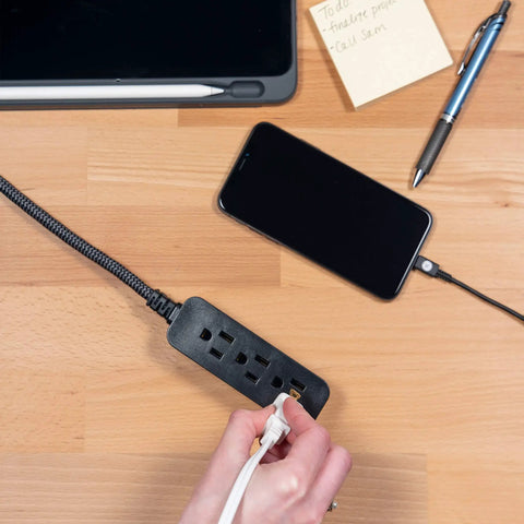 Person plugging into 3 Outlet Power Strip With 15 Ft Braided Cord Flat Plug 250 Joules Surge Protector UL Listed Black 5 Pack on desk