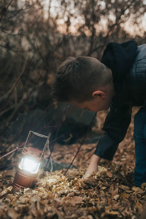 Child examining ground lit by 4 Pack Multicolor Camping Lanterns, Ultra Bright LED Tent Lights for Power Outages, battery powered.
