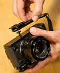 Micro Clutch L Plate Hand Strap for Mirrorless Cameras shown with battery access and ARCA base on wooden surface