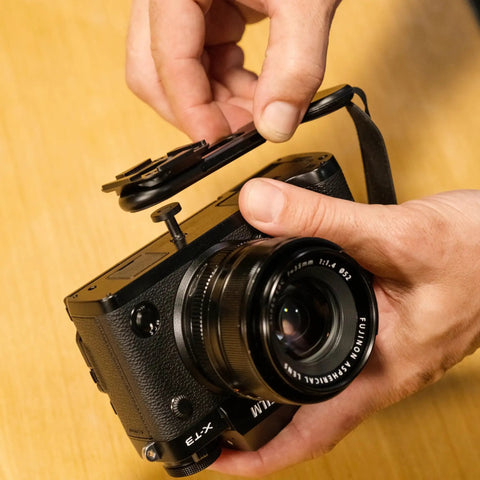 Micro Clutch L Plate Hand Strap for Mirrorless Cameras shown with battery access and ARCA base on wooden surface