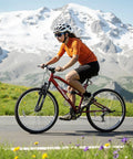 Cyclist riding a 26 Inch Mountain Bike With Dual Suspension For Men Women And Adults on a scenic mountain road, snow-capped peaks in background