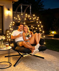 Two Person Outdoor Hanging Egg Chair With Stand And Adjustable Footrest Oversized Wicker Swing Chair With Thick Cushions For Indoor And Outdoor Chill Cozy Relaxing Black With Footrest And Light, showing two people sitting, illuminated at night.