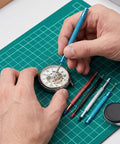 Round Leather Movement Holder With Cushion and Six Piece Watch Hand Tool Kit used for precise watch repair on a green mat.