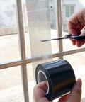 Person using scissors to cut Heavy Duty Window Screen Repair Tape And Mesh Patch Kit 2 Inches By 16 Feet Long Black adhesive strip.