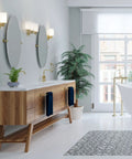 Modern bathroom with Latitude II 24 Inch Wall Mounted Towel Bar In Brushed Brass, wooden vanity, round mirrors, and green plant.
