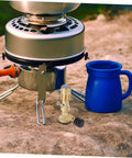 Outdoor setup with Flame Bunsen Burner Portable Gas Blowtorch Head For Propane Cooking Stove, metal stove, and blue mug on rock