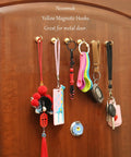 Crazy Strong Magnetic Hooks Pack Of 6 Heavy Duty NdFeB Magnets With Hooks For Refrigerator Cabinets Grills And Outdoor Gear Golden Finish Perfect For Home Organization Dorm Rooms Office Spaces Kitchen And Garage Or RV Use hanging on a wooden door holding keys and lanyards.