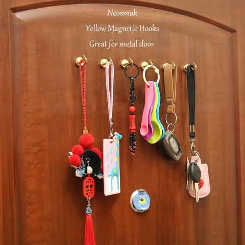 Crazy Strong Magnetic Hooks Pack Of 6 Heavy Duty NdFeB Magnets With Hooks For Refrigerator Cabinets Grills And Outdoor Gear Golden Finish Perfect For Home Organization Dorm Rooms Office Spaces Kitchen And Garage Or RV Use hanging on a wooden door holding keys and lanyards.