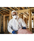 Person wearing All In One N95 Respirator For Sanding Drywall Painting And Woodworking With Exhalation Valve Directing Air Downward 10 Pack For Dust Fiberglass Particles And Non Oil Based Aerosols, handling insulation in construction site