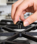 Hand installing 16 Piece Stove Grate Rubber Feet Set 5304475129 Replacement for Gas Ranges on black cooktop grid.