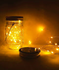 Lit Solar Mason Jar Lights 4 Pack With 30 LEDs Starry Fairy String Hanging Jar Lights glowing in dim light with jar and lid visible