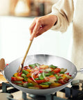 Cooking vegetables in Go-To 14-Inch Carbon Steel Wok With Bamboo Handle For Stir Frying, Sauteing, Steaming, Braising And Deep Frying.