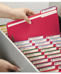 Hand holding letter size red fastener folder with assorted tabs in a filing drawer, ideal for hustle free filing.