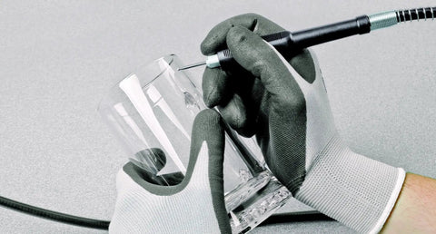 Close-up of hands with gloves using a tool to engrave a glass, showcasing detail and precision work.