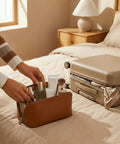 Brown medium Travel Makeup Bag For Women With Large Capacity, Waterproof Cosmetic Pouch on bed next to suitcase.