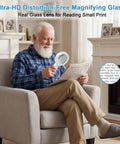 Senior man using Crystal Clear Lighted Handheld Magnifier With 12 LEDs for reading a newspaper in a cozy living room setting.