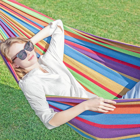 Person relaxing in colorful hammock on grass, emphasizing Double Hammock With Stand For Outdoor Use Upgraded Spreader Bar Heavy Duty Steel.