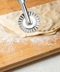 2-piece zinc-alloy pizza cutter wheel set with fluted edge on long handle cutting dough on a wooden board.