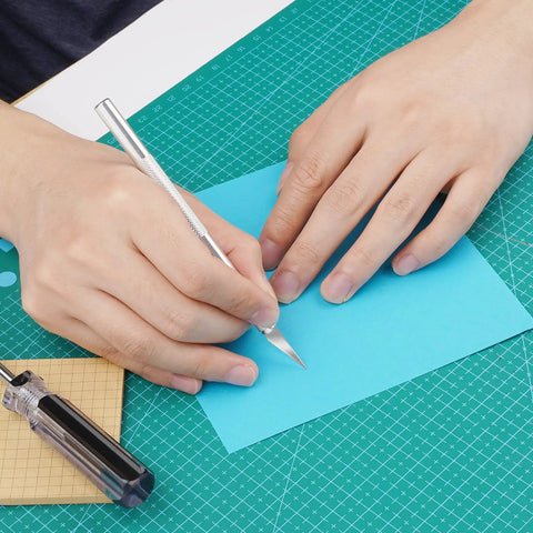 Person using Pro Grade Number Eleven Exacto Knife Blades Set for cutting blue paper on green cutting mat