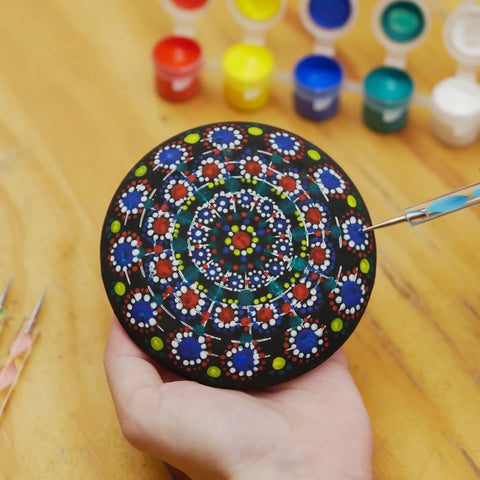 Rock Painting Kit With Dotting Tools And Stencils And Acrylic Paints For Easy At Home Relaxing DIY Arts And Crafts Includes 5 Wooden Rocks 6 Mandala Stencils 12 Vibrant Colors And All The Dotting Tools For Adults And Women, showing a hand-painted mandala stone with dotting tool and paints.
